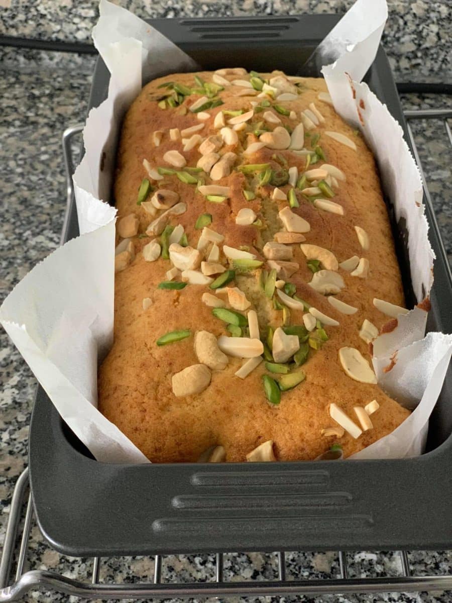 Freshly baked mava cake topped with almonds and green toppings in a baking tin. Photo credit: Diana Vesuna