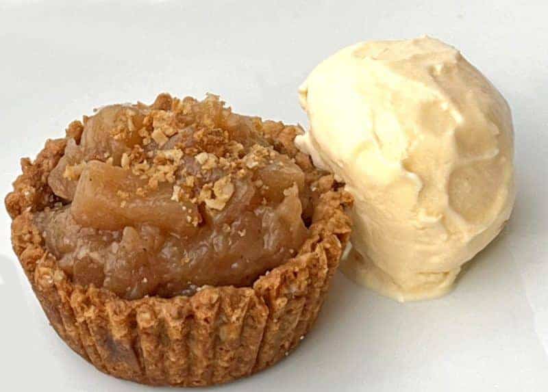 A close-up of an apple pie cookie cup next to a scoop of creamy vanilla ice cream.