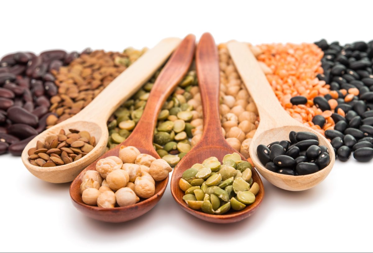 Close-up of wooden spoons holding various types of beans against a contrasting background.