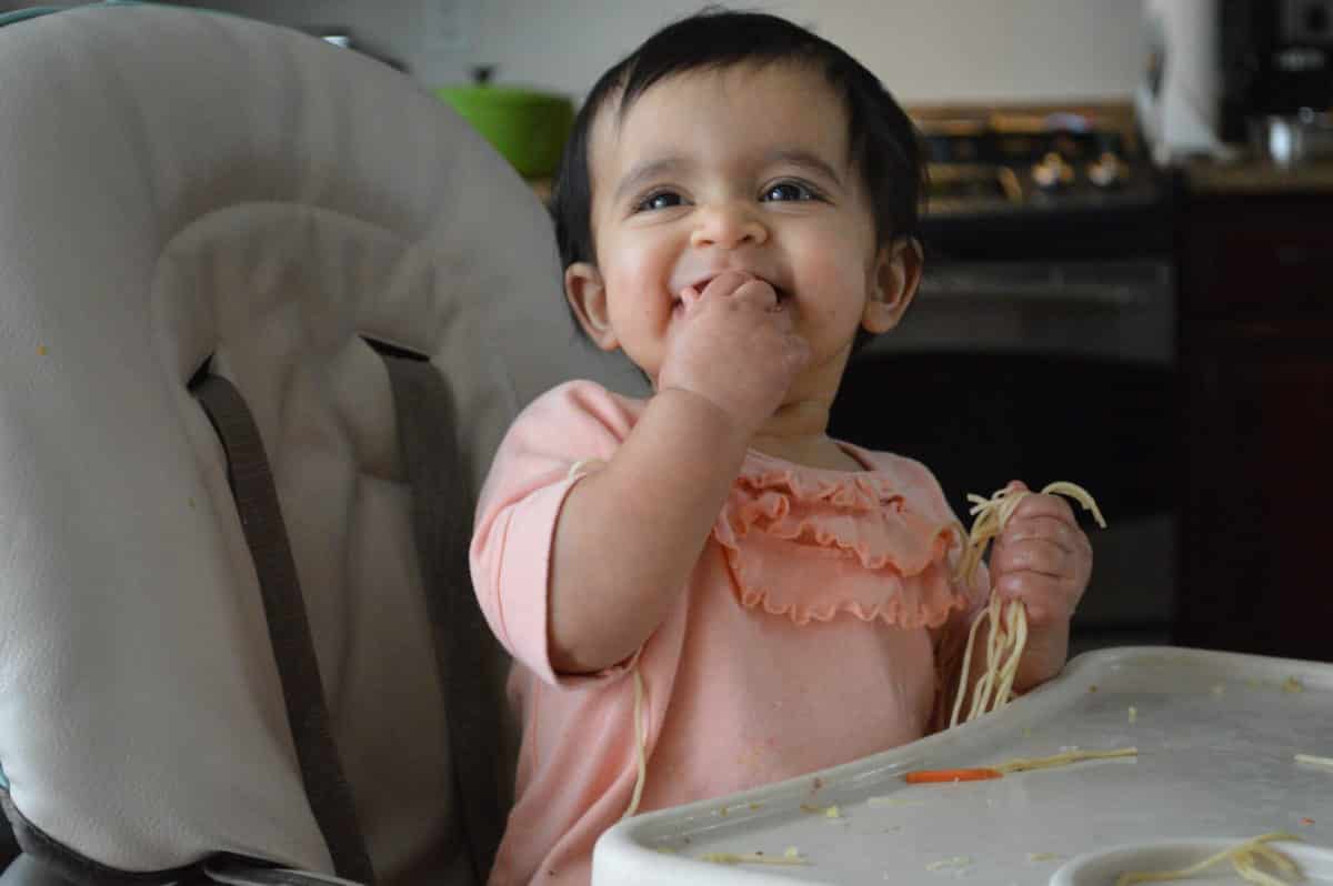 A baby eating and enjoying her food in a high chair.