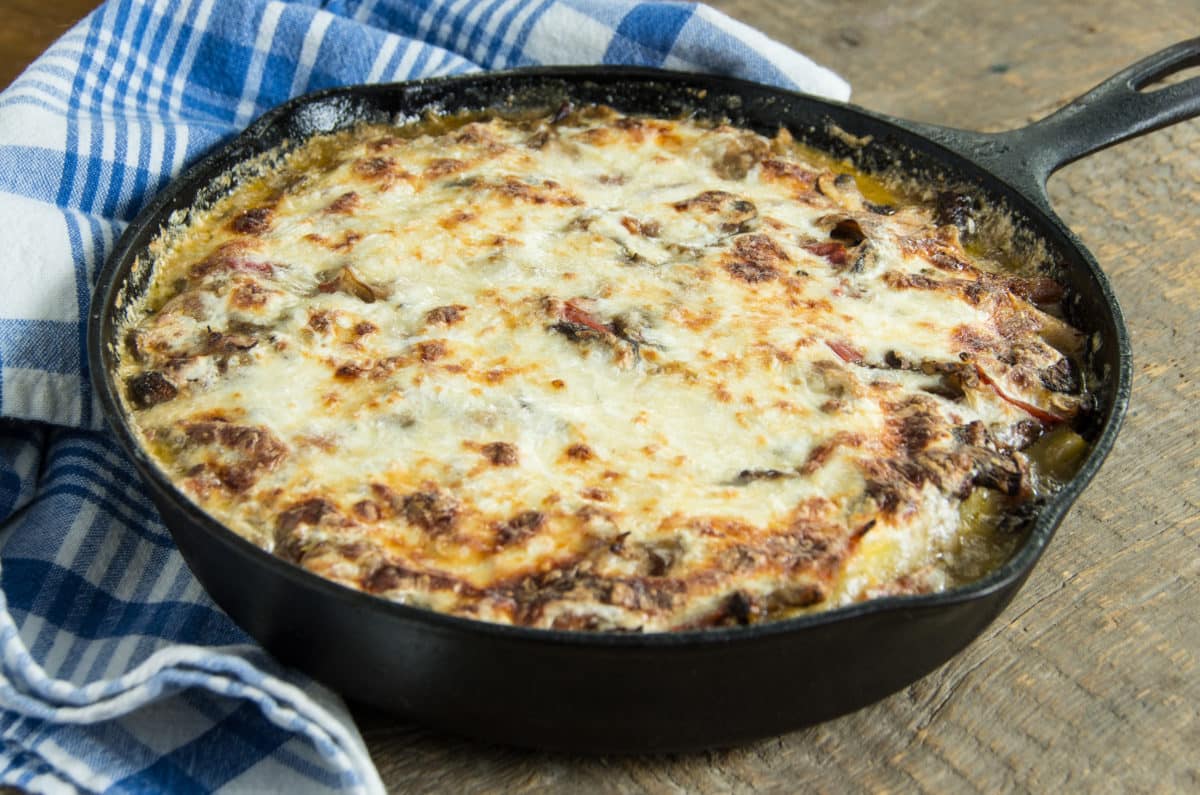 Golden-brown polenta pie with melted cheese and toppings in a cast iron skillet.