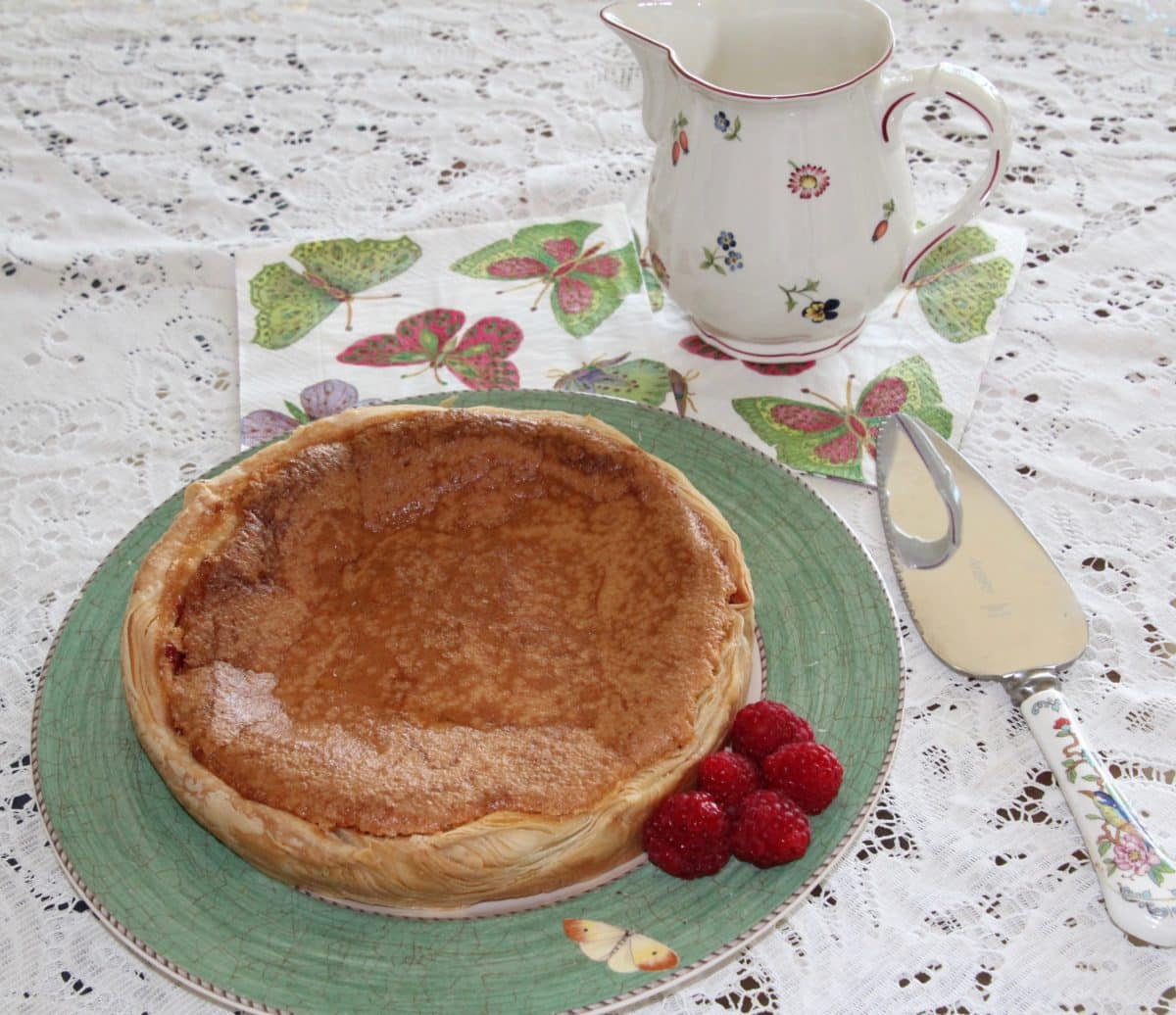 Bakewell Pudding on a plate with raspberries and a teapot.