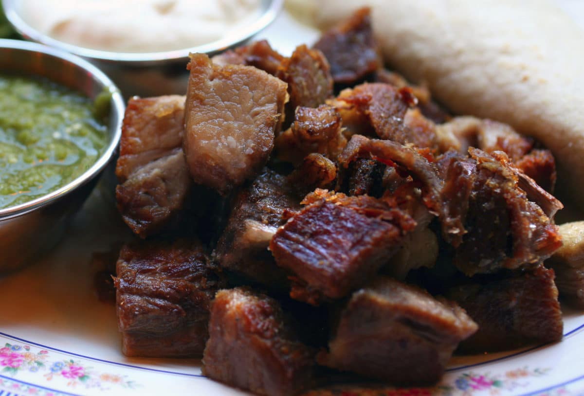 A plate of barbecued goat meat chunks served with dipping sauces on the side.