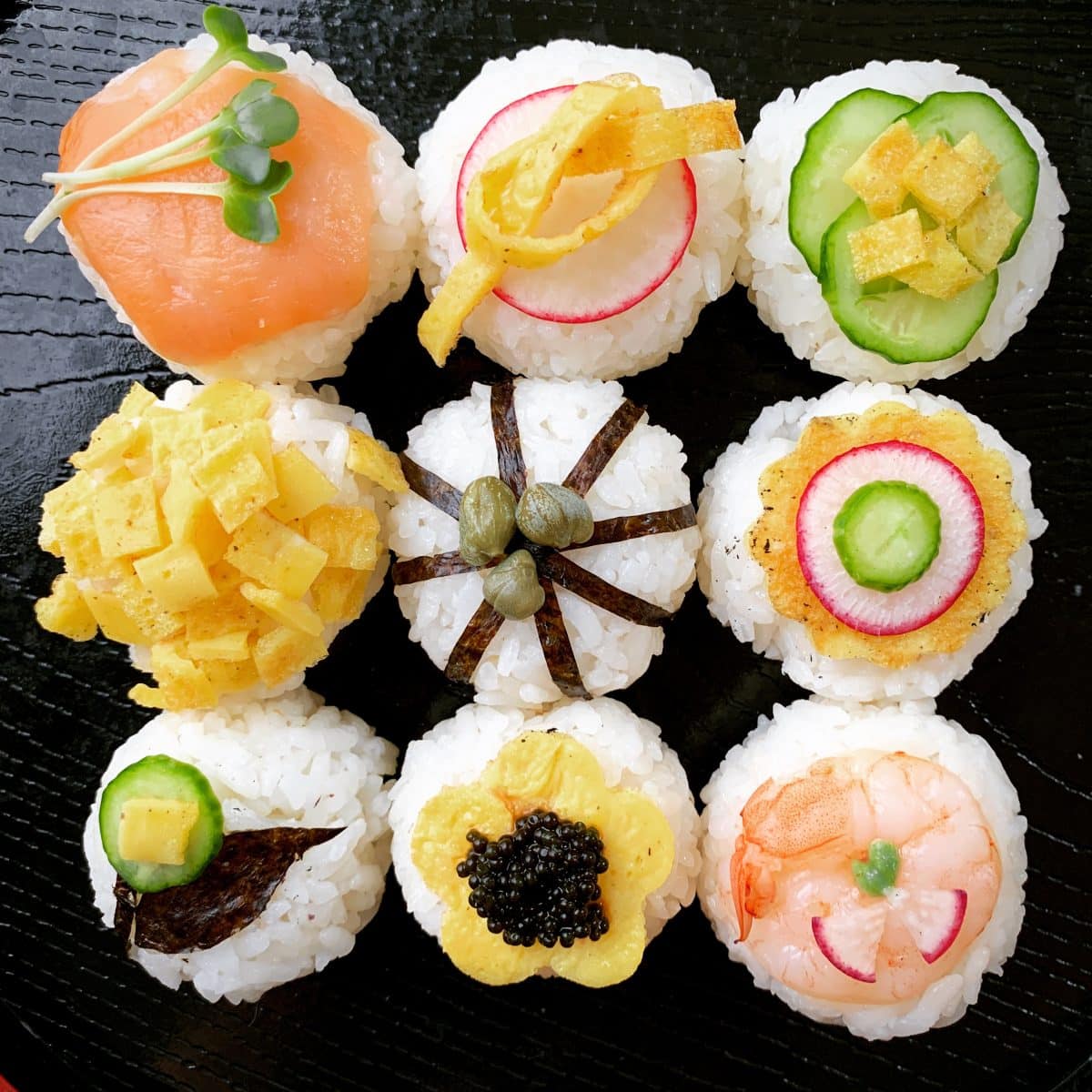 Assorted breakfast temari sushi on a black plate.