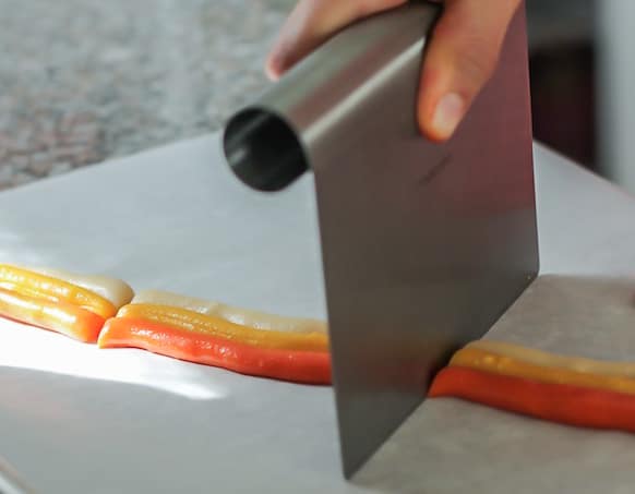 Hand using a large knife to slice candy corn pieces.