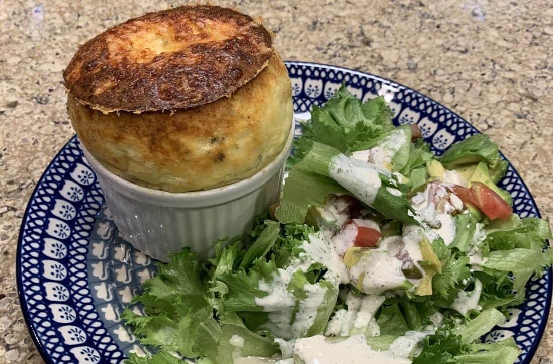 A risen cheese and corn soufflé served next to a fresh salad on a blue and white patterned plate.