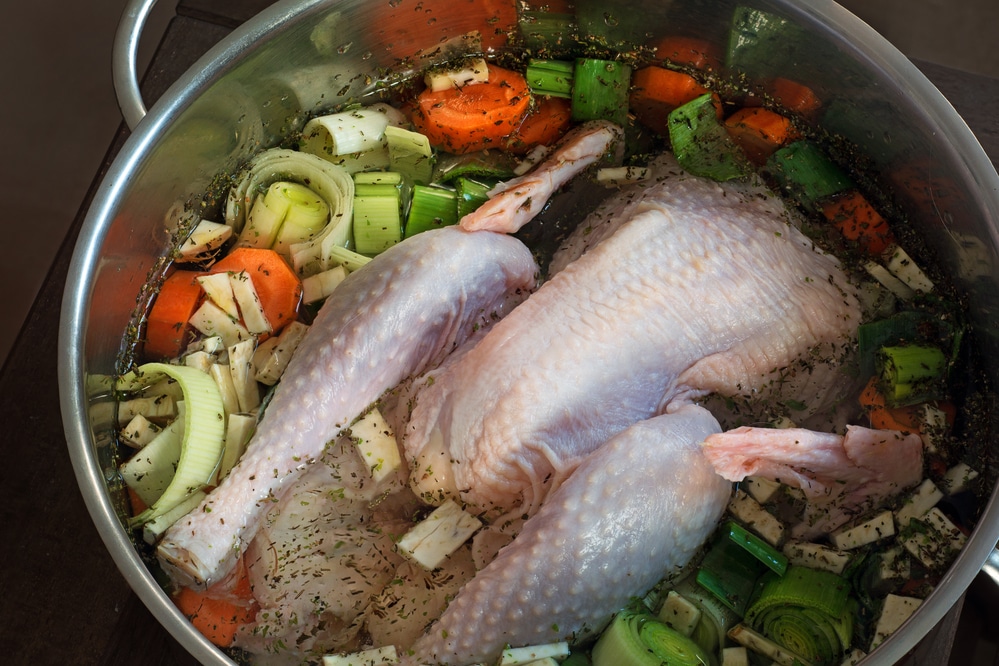Fresh chicken and vegetables being prepared in a pot for making chicken broth.