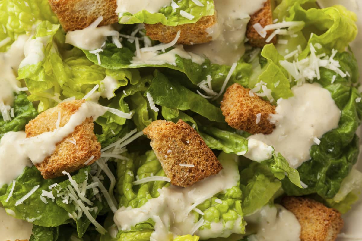 Close-up view of a Caesar salad with shredded cheese and golden croutons.