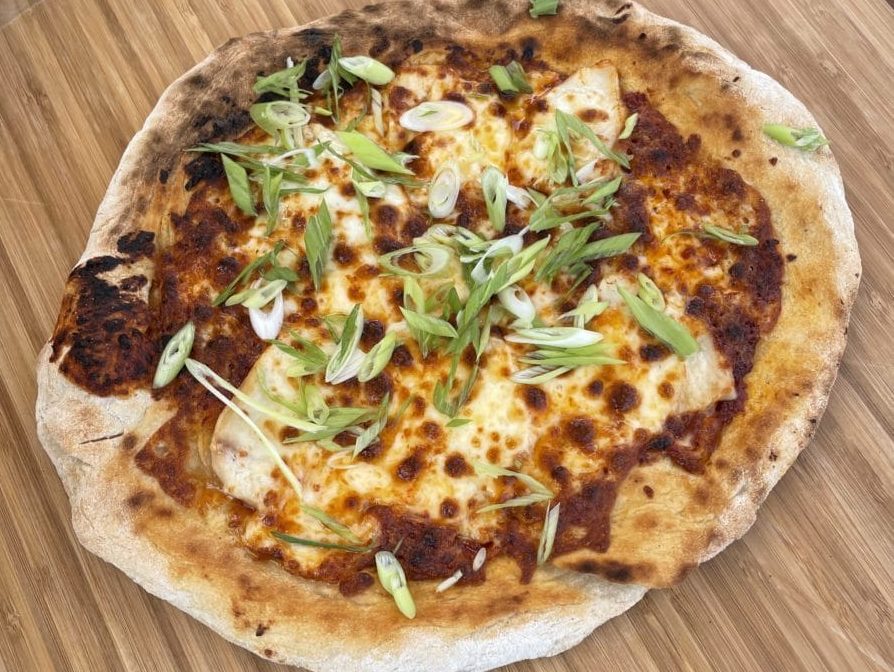 Freshly baked pizza with chicken, cheese, and green garnish.