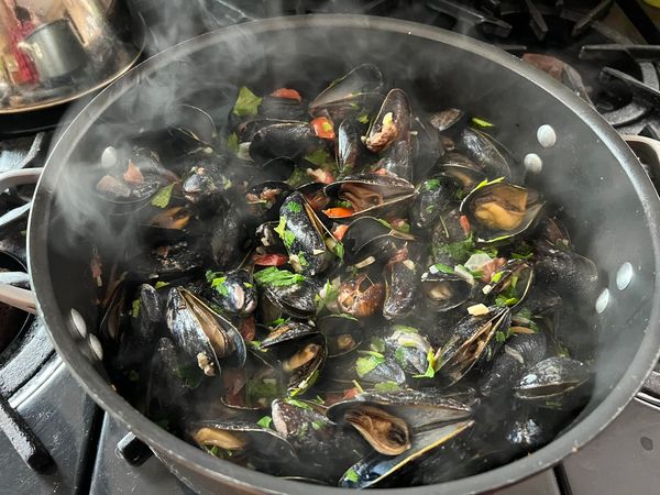 Mussels being cooked with herbs in a pot.