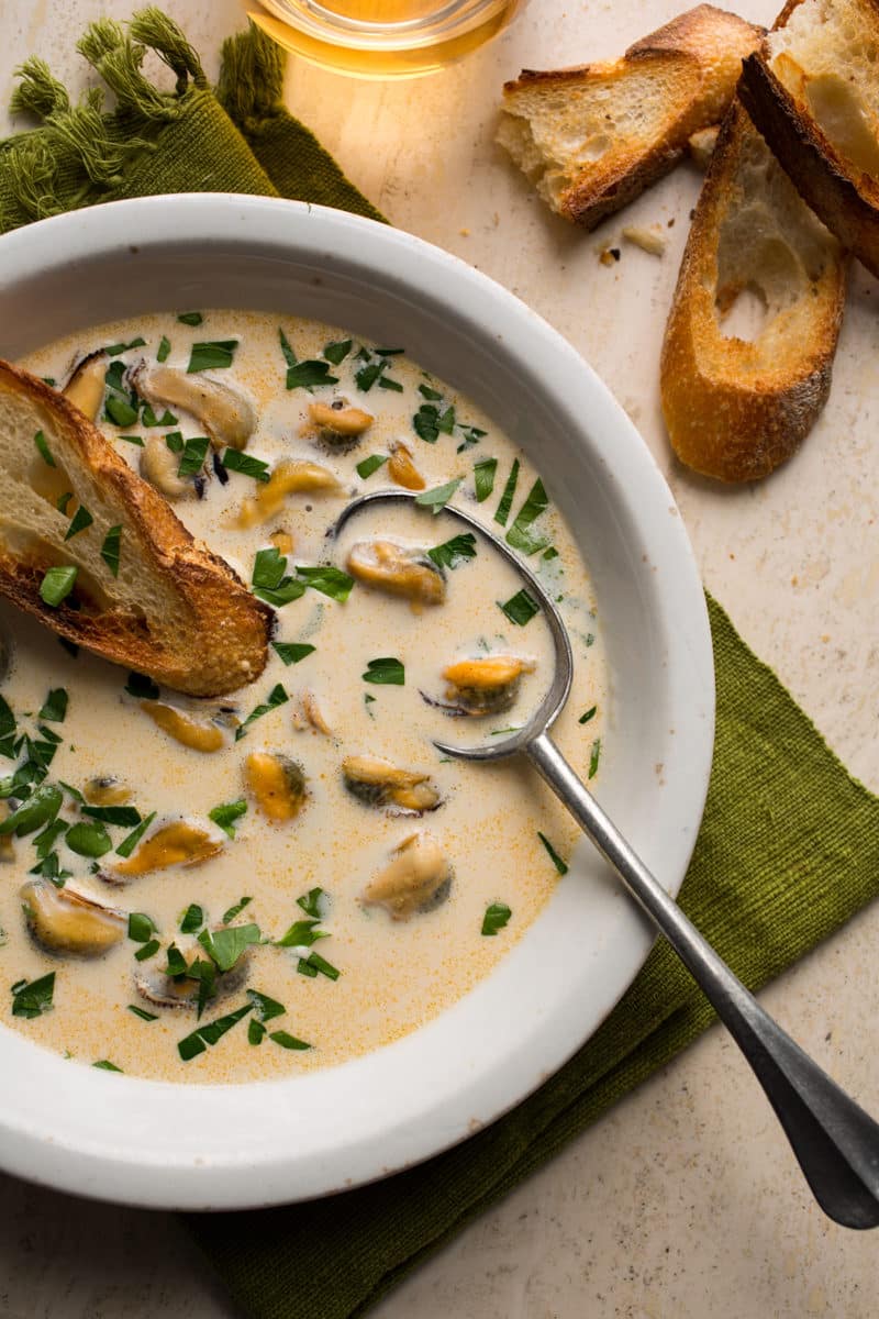 Creamy chowder served in a white bowl with a silver spoon, accompanied by slices of crusty bread.