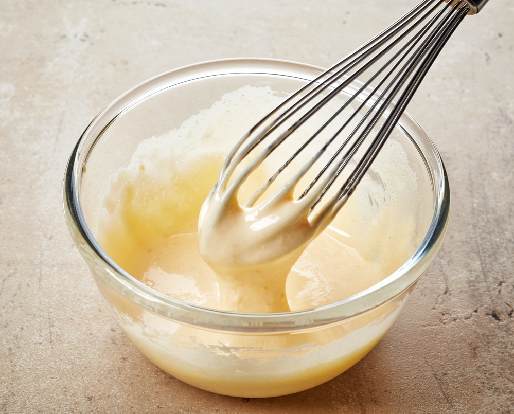 Whisk stirring rich and creamy Tahini Hollandaise sauce in a bowl.
