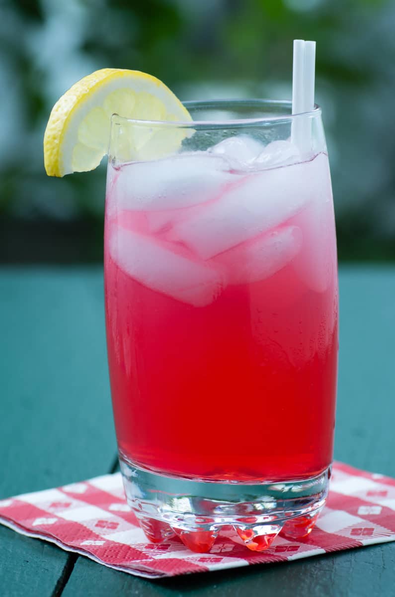 A red Diabolo cocktail with a lemon slice and straw.