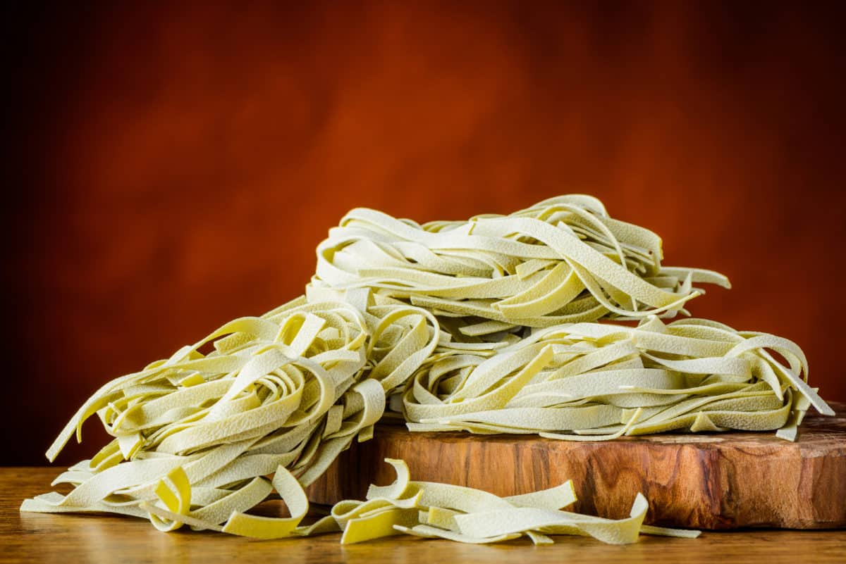 Strands of green fettuccine pasta on a wooden board.