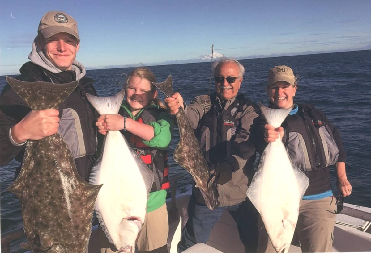 Four individuals holding large fishes, showcasing their catch on a boat with the ocean in the background.