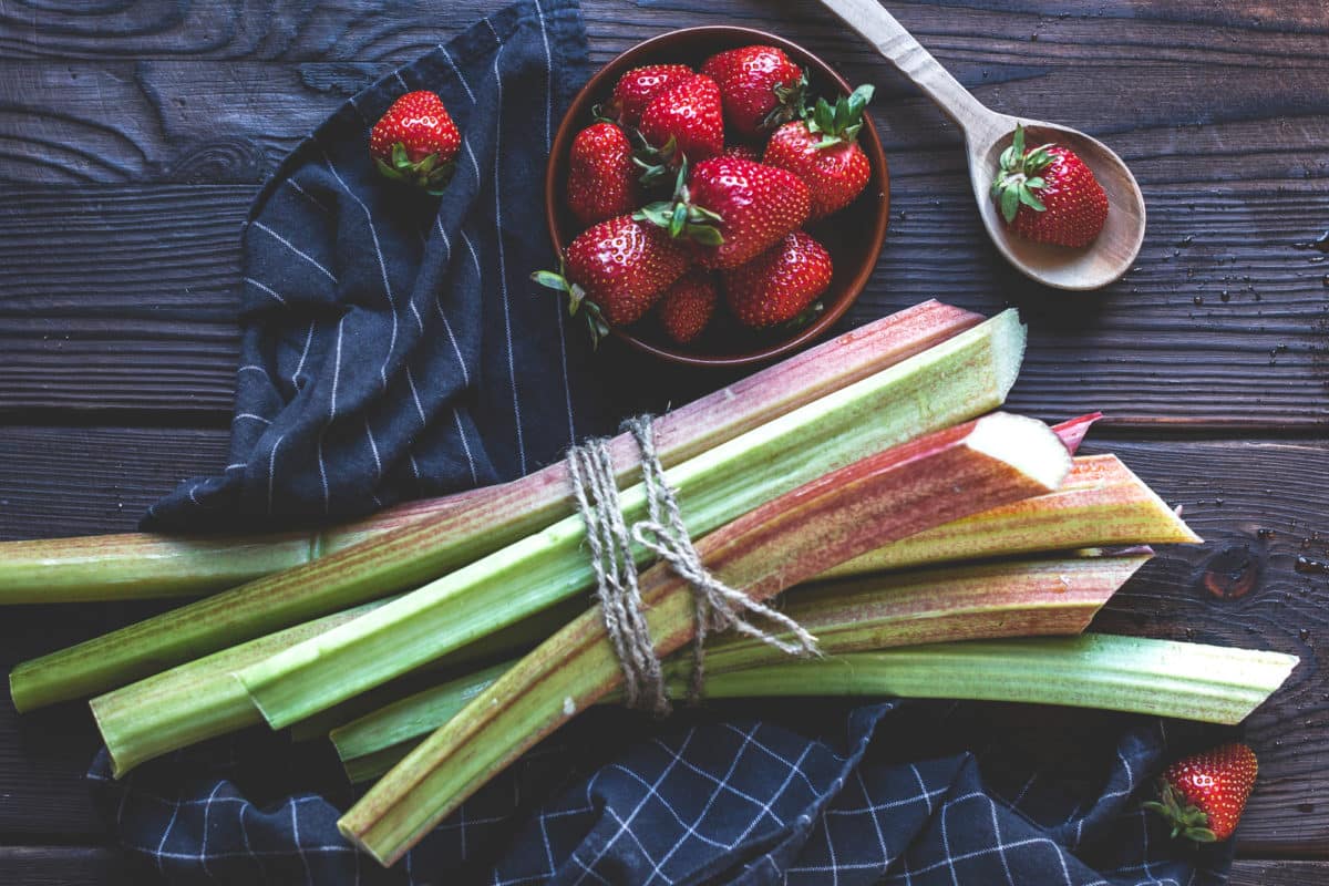 A bowl of fresh strawberries next to tied rhubarb stalks.