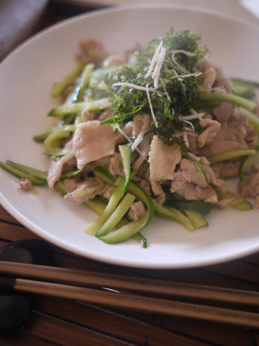 White plate containing fried pork garnished with ginger, greens, and cheese shavings on top.