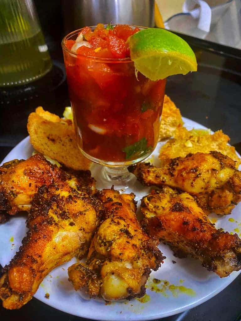A tantalizing serving of chicken wings alongside a glass of zesty salsa topped with a lime wedge.