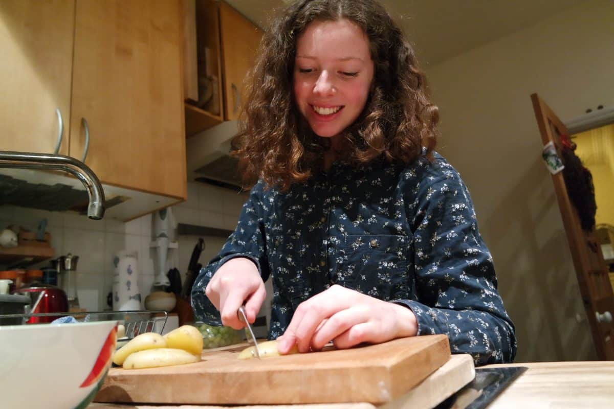 Young girl diligently cutting vegetables on a wooden chopping board