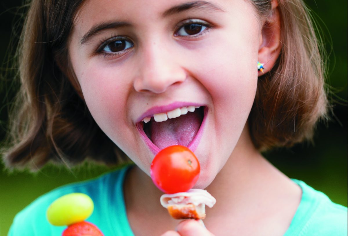 A joyful girl tasting a colorful lunch skewer.