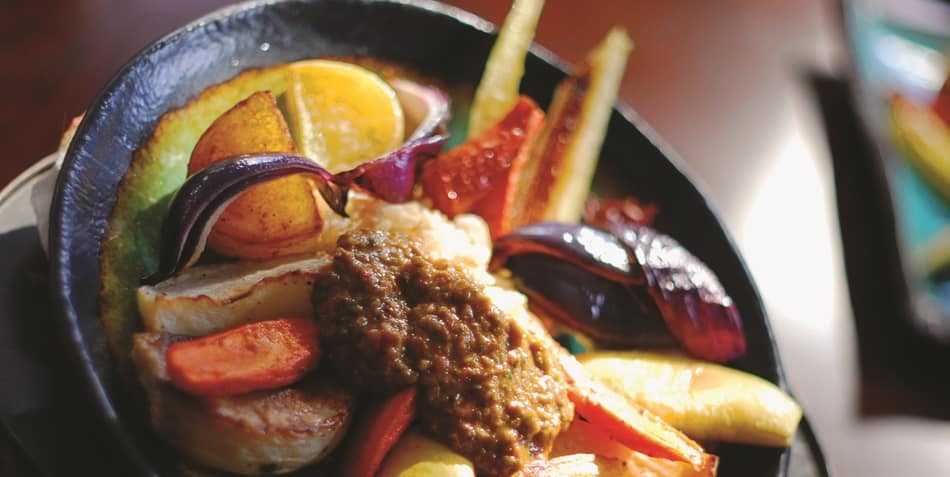 Colorful meal with Harissa sauce, vegetables, and meat.