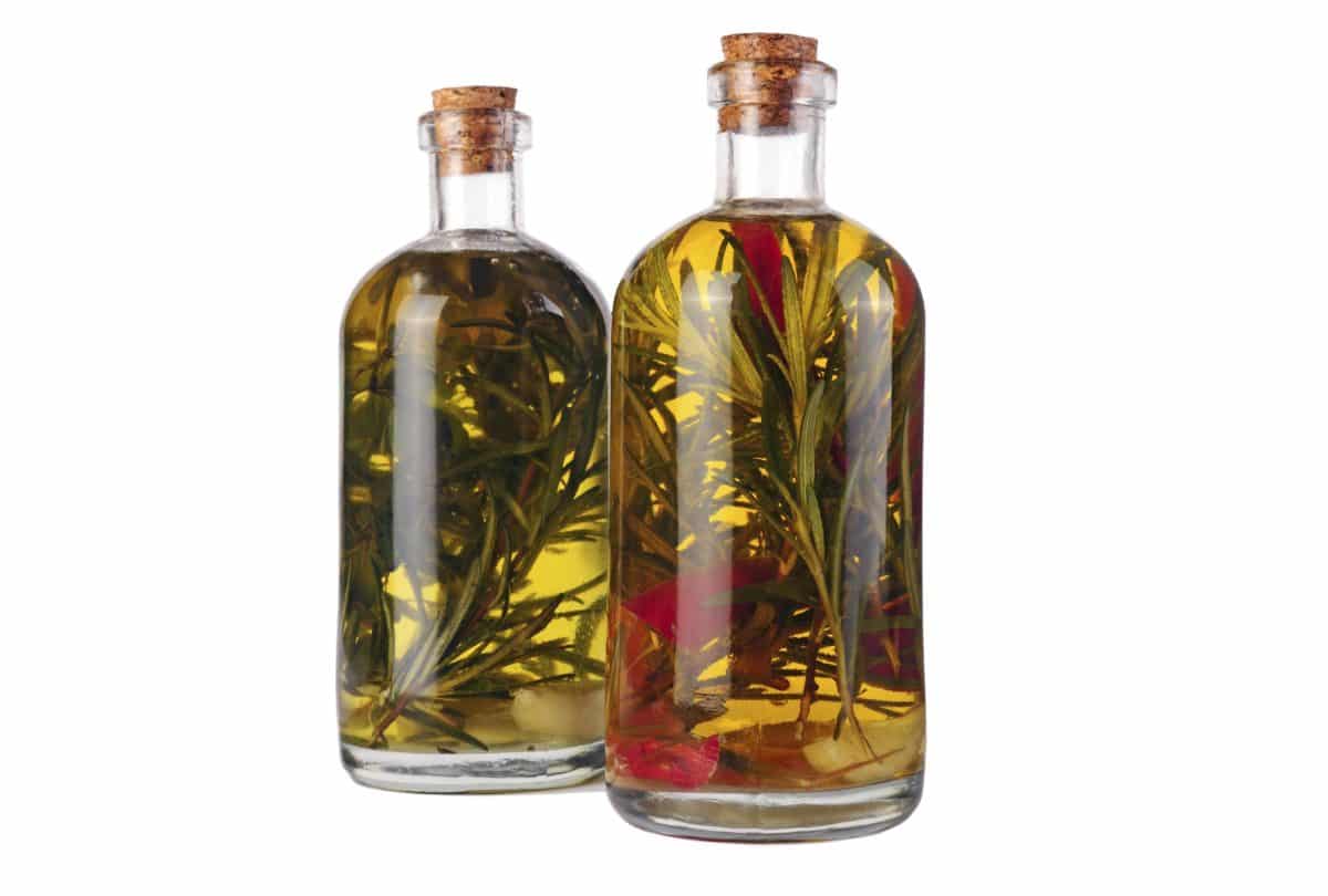Two transparent bottles filled with oil and infused with vibrant herbs.