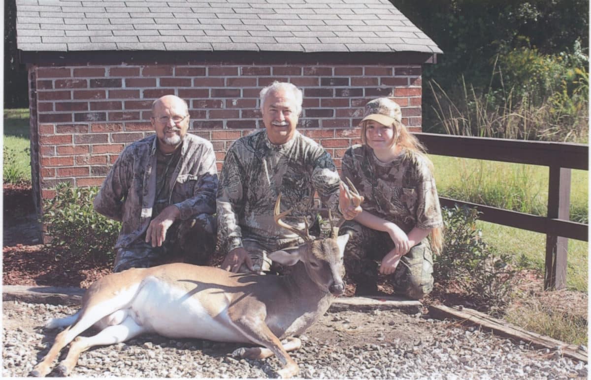 Three hunters proudly displaying their hunted deer in front of a brick building.