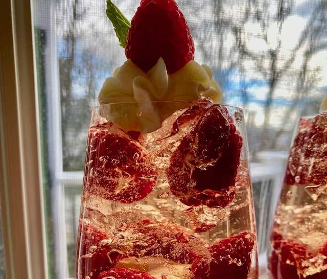 Close-up of jelled prosecco dessert topped with raspberries and crème fraîche whipped cream in a glass.