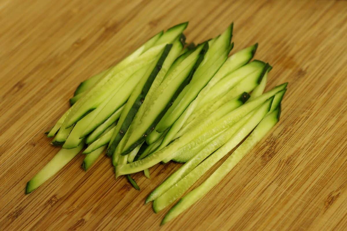 Freshly julienned cucumbers on a wooden cutting board.