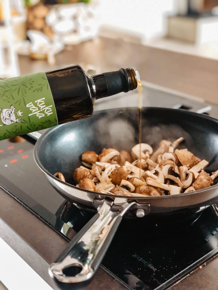 Olive oil being poured into a frying pan with mushrooms
