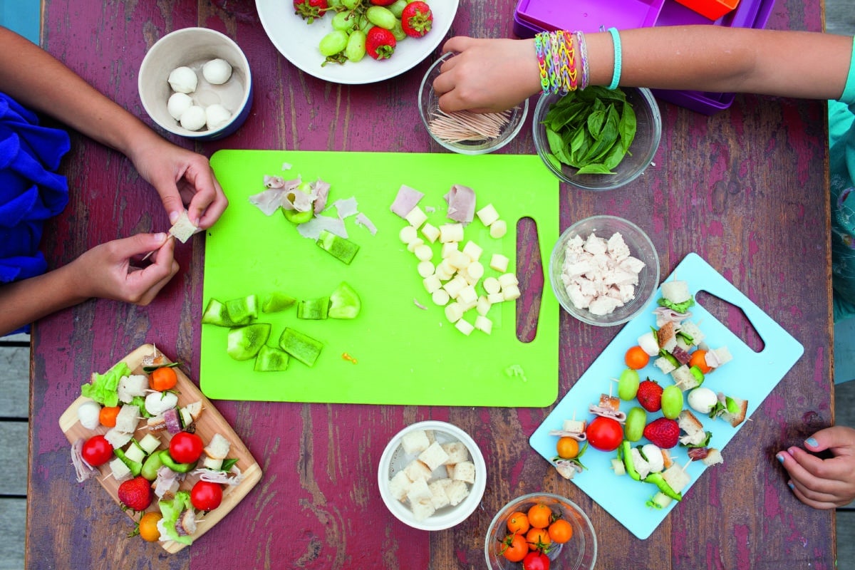 Children's hands assembling various ingredients onto skewers.