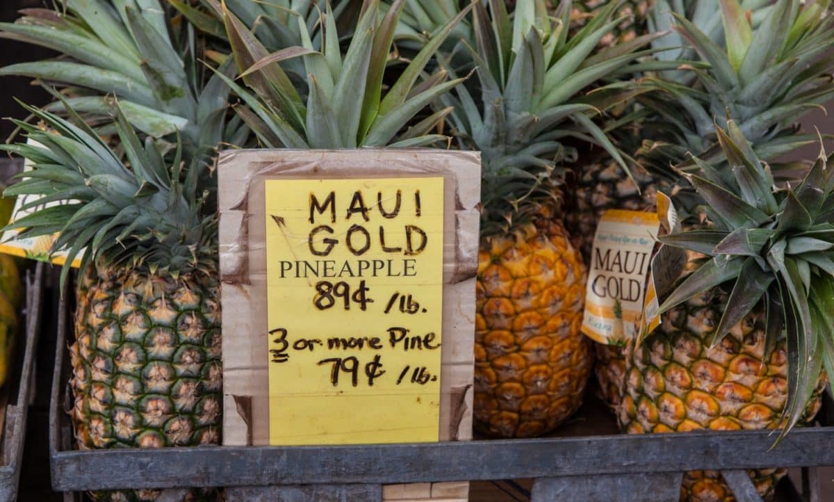 Fresh Maui Gold pineapples for sale at a Hawaiian farmer's market with price tags.