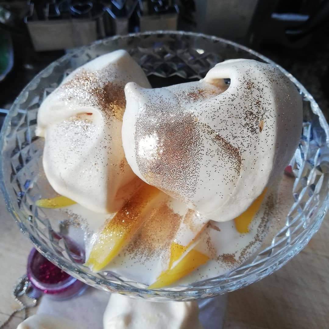 Close-up of meringues topped with peaches, cream, and edible glitter.