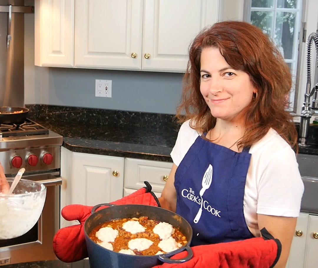 Michelle Siudut, co-host, holding a pot of Buffalo Chili with Dumplings in a kitchen setting.