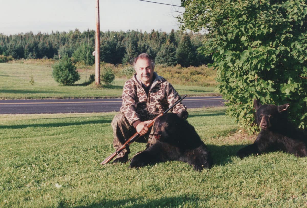 Mike Yacino proudly posing with a rifle next to a hunted bear.