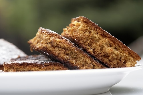 Slice of gingerbread cake on a white plate with a dusting of powdered sugar.