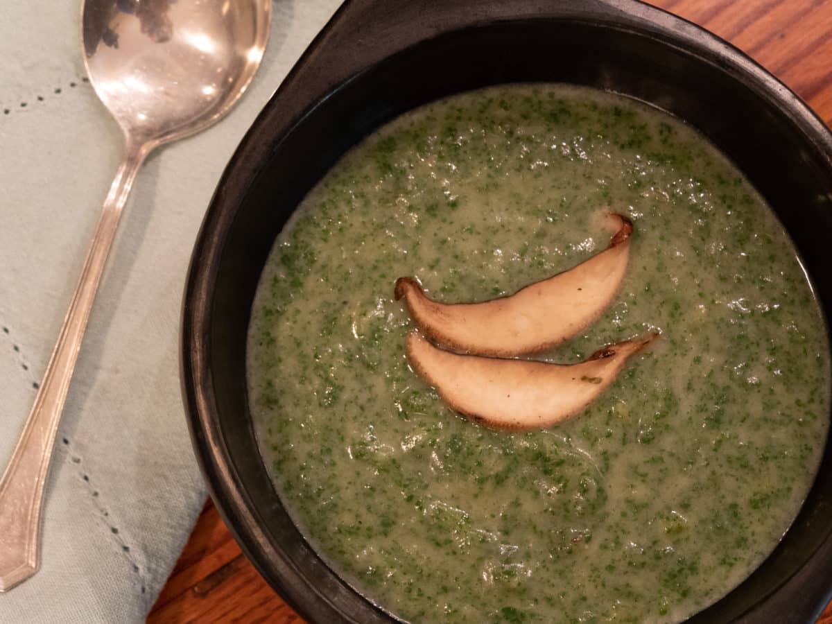 Close-up of a black bowl containing green nettle soup, garnished with two slices of sautéed mushrooms.