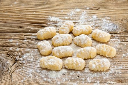 Freshly made potato gnocchi on a wooden surface sprinkled with flour.