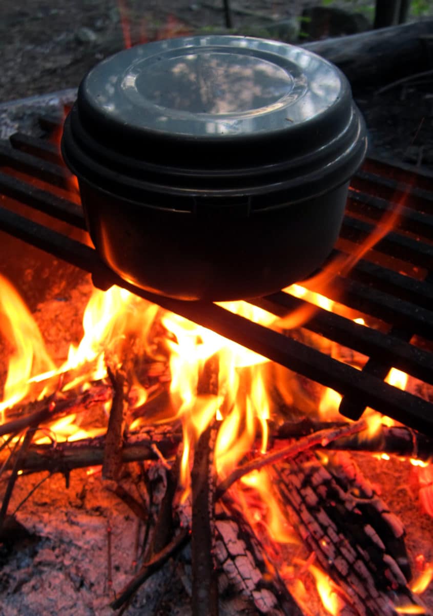 Black pot positioned over a roaring open flame for outdoor cooking.