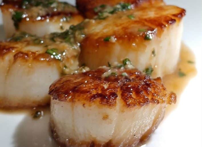 Close-up of golden-brown pan-seared scallops with herb wine sauce.