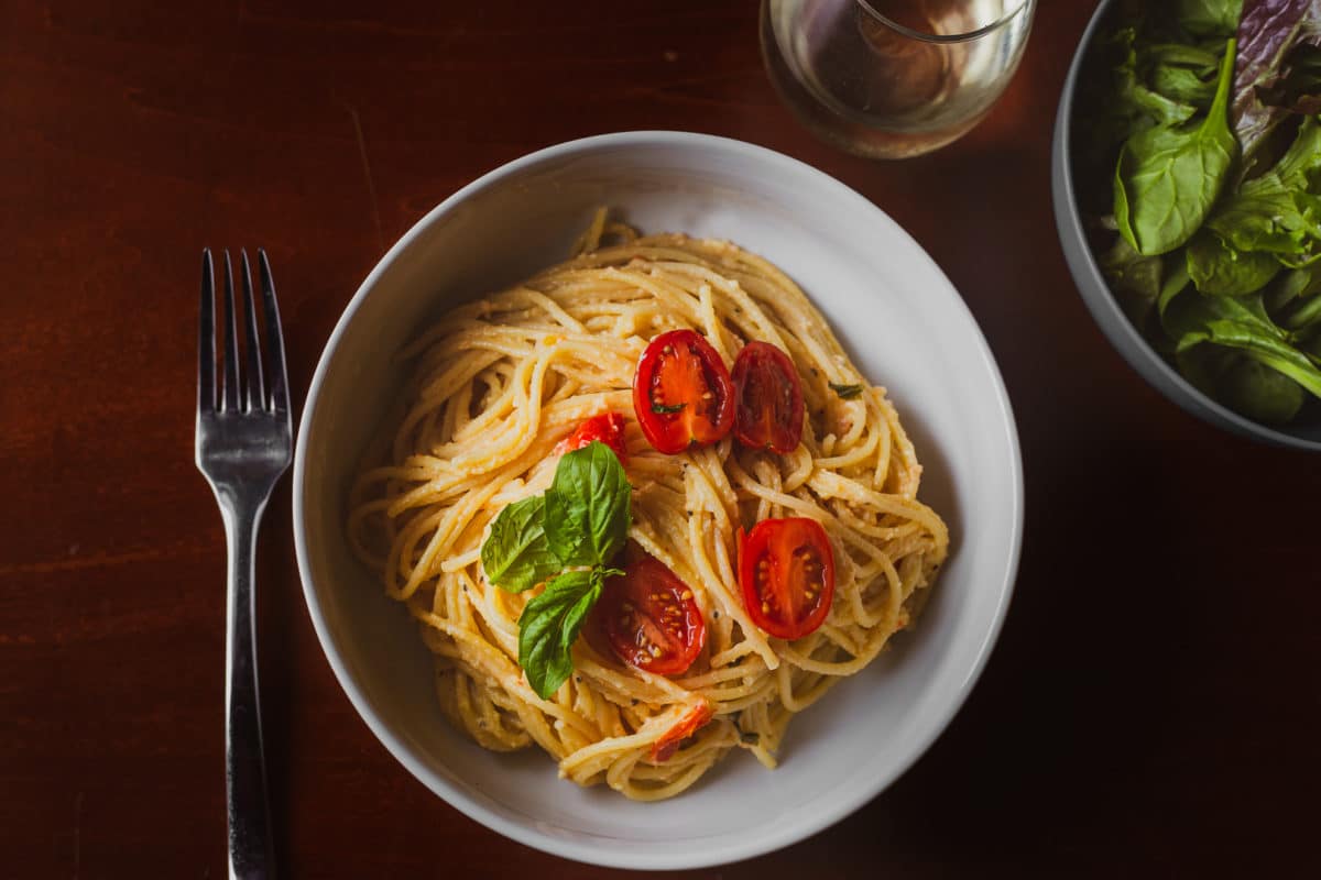 A bowl of pasta garnished with tomato slices and basil leaves.