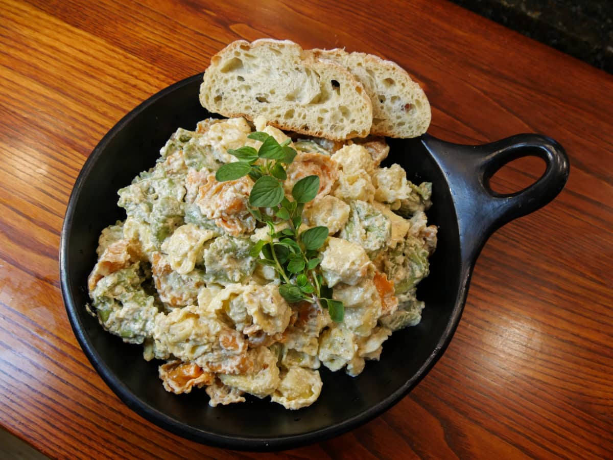Pasta covered in rich walnut sauce, served in a black bowl with a side of sliced bread.