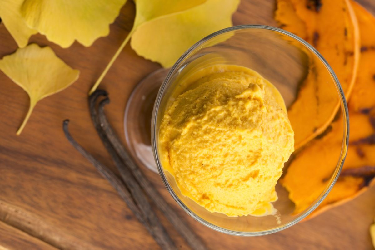 A scoop of pumpkin ice cream beside vanilla beans and autumn leaves.