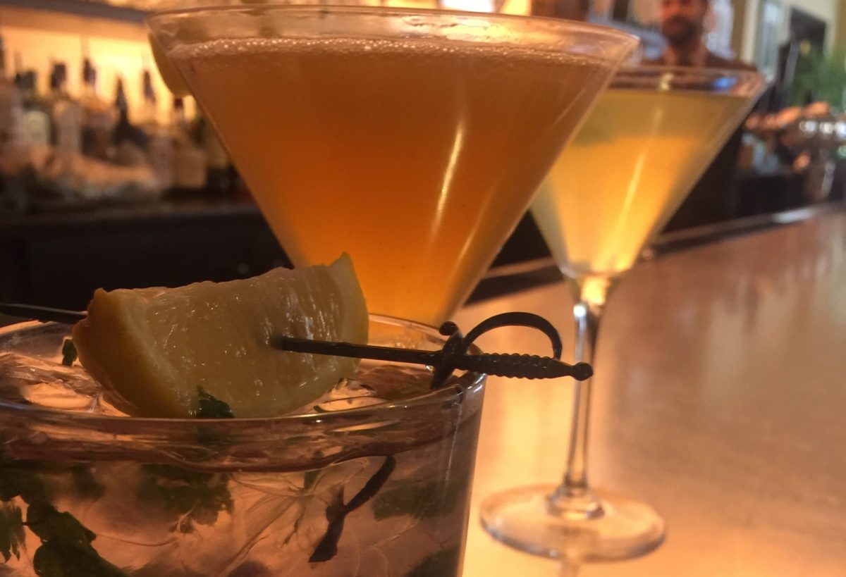 Two cocktail glasses filled with golden beverages and garnished fruit.