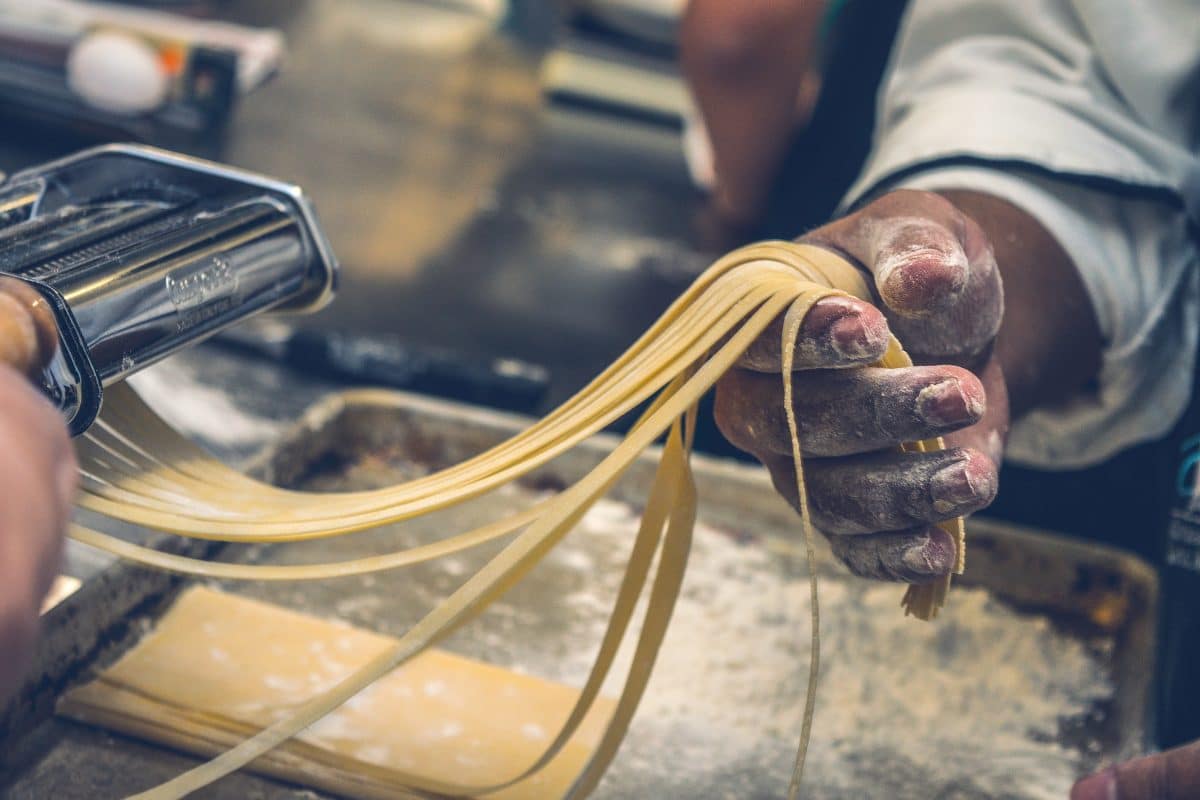 Close-up of a hand using a machine to create rolled pasta.