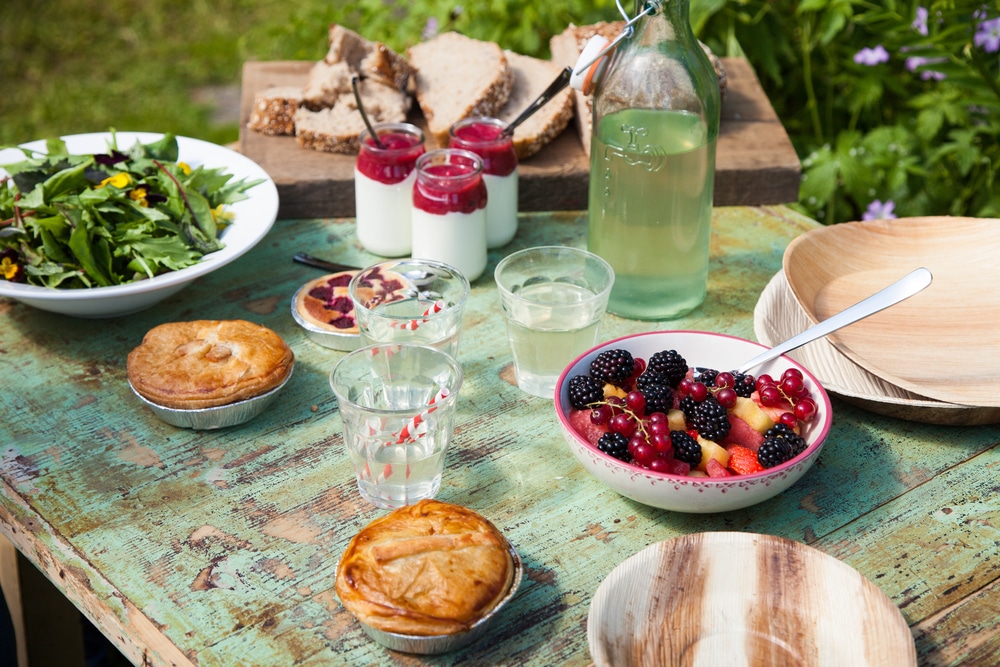 Outdoor table set with fresh fruits, salads, drinks, and pastries for a picnic.