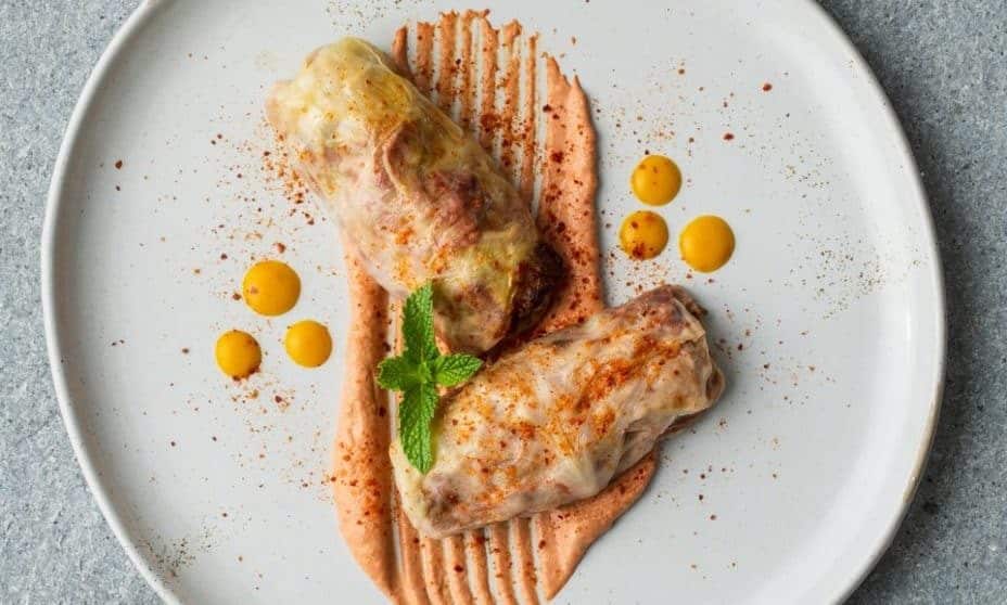 Two holishkes served on a plate with sauce and garnish.