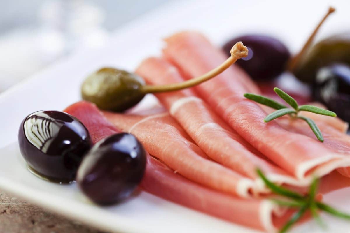 Rolled serrano ham garnished with rosemary and olives on a plate