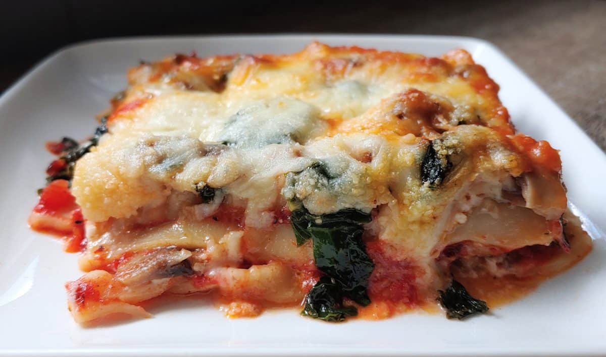Slice of lasagna revealing layers of mushroom, kale, and cheese.