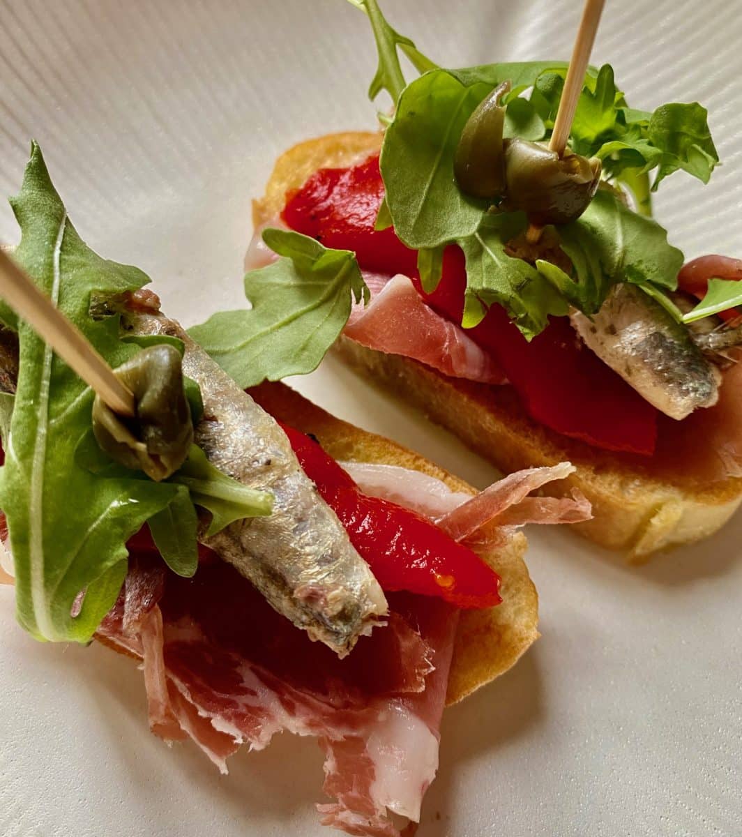 Closeup of Spanish tapas with fish, ham, and arugula.